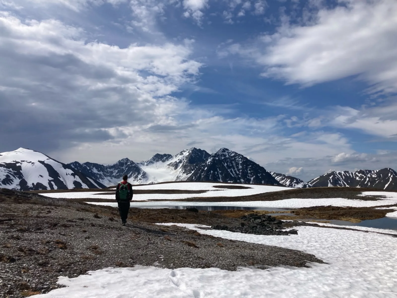 A geologist crossing a snow-patched plateau towards a snowbound range